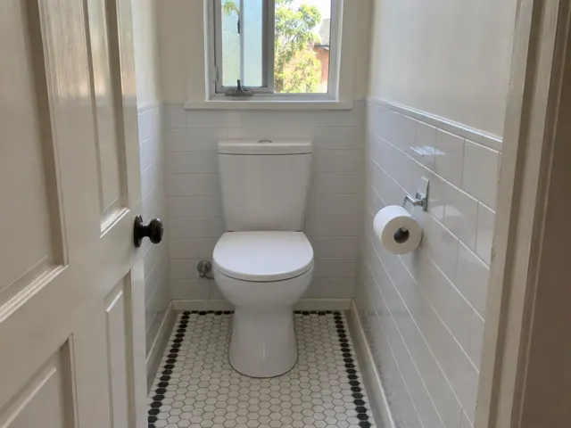 Clean white toilet in a tiled bathroom with a window and patterned floor in Pennant Hills