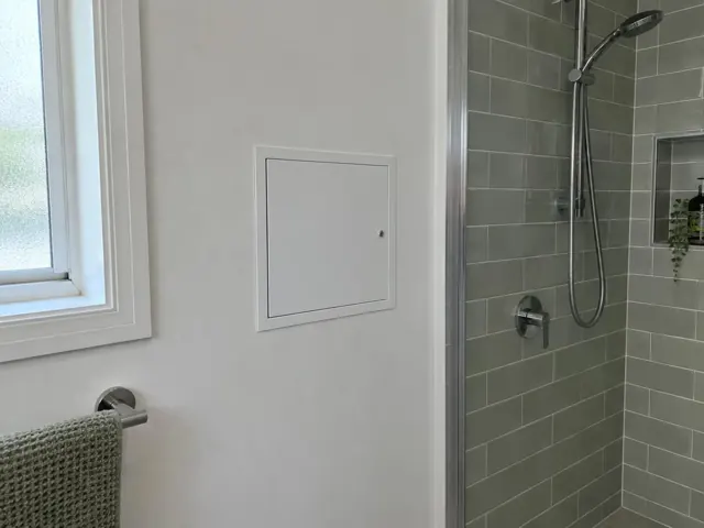 Bathroom wall with a small access panel beside a tiled shower and window in Thornleigh